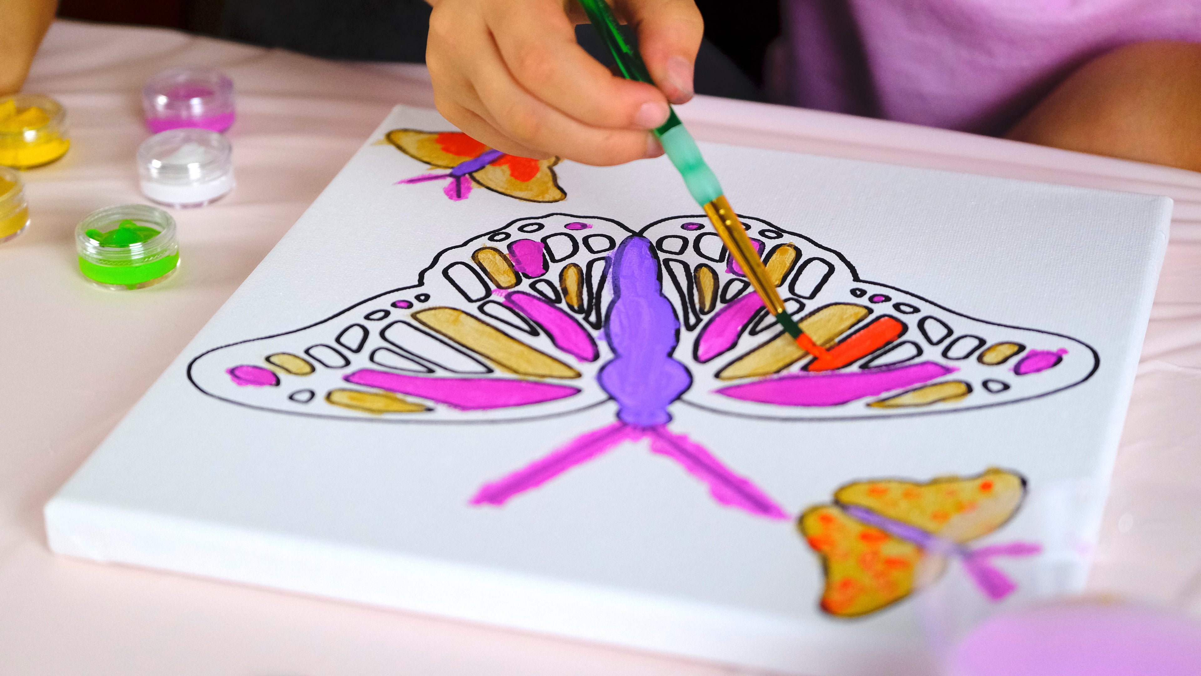 Child painting a butterfly design on a canvas with colorful paints.